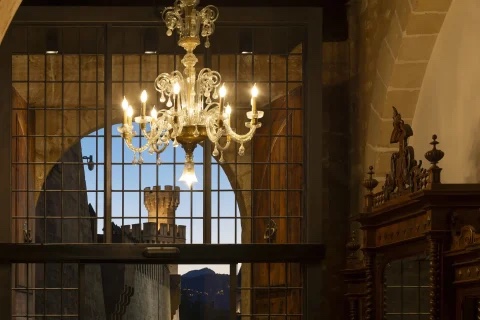 A Venetian-glass chandelier in a Gothic-vaulted room, with Palma Cathedral's tower visible through an iron-barred window in the background
