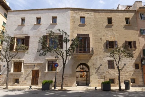Hotel Can Cirera in daylight: the 15th-century stone palauet with its arched entrance, wooden shutters and honey-coloured marès facade on a Palma cobbled square