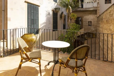 A private terrace balcony with wicker chairs and a small table, looking out onto the stone lanes of Palma's old town in warm afternoon sun