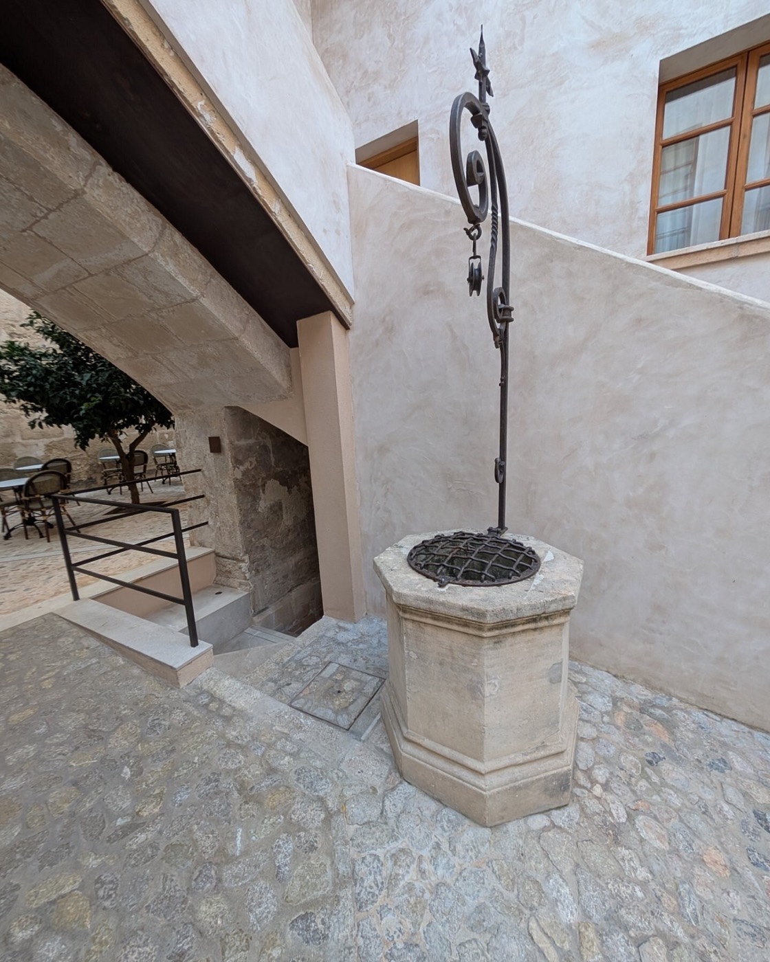 A weathered stone well-head standing in the corner of the paved courtyard against marès walls
